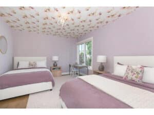 Streeter built purple bedroom with two double beds, flowers painted on the ceiling, large window, hardwood floors and rug.